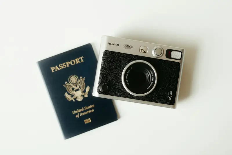 A passport and a camera laid out on a white surface, ready for travel